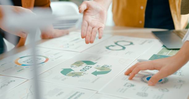 Closeup of team members examine ESG-related documents, pointing and discussing investment strategies for sustainable and renewable energy resources. Eco-Friendly Business Discussing ESG Goals concept.