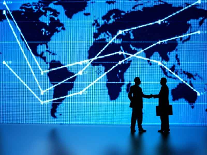 Two business professionals shaking hands in front of a global market screen symbolizing international cooperation and building investor confidence.