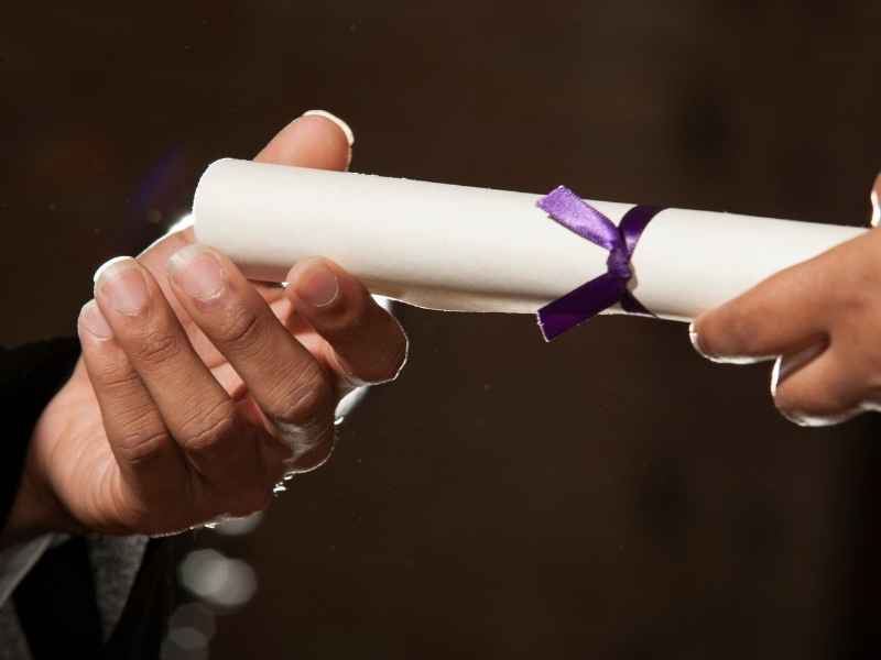 Hands exchanging a diploma symbolizing graduation, scholarships, and education-to-employment transition