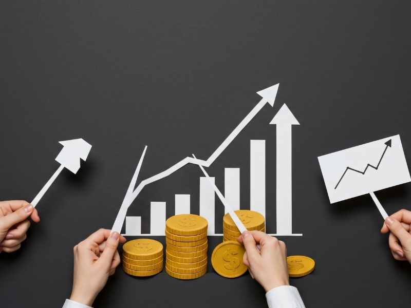 Stacks of coins in front of a rising chart and arrows on a blackboard, symbolizing economic growth.