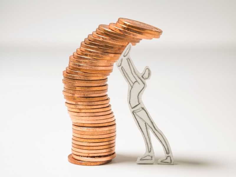 Stacked coins leaning while a person supports them, symbolizing the need for a cash buffer and stability.