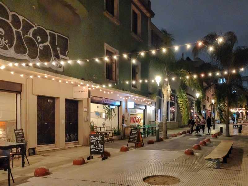 Outdoor dining area on a pedestrian-friendly street at night with string lights overhead.
