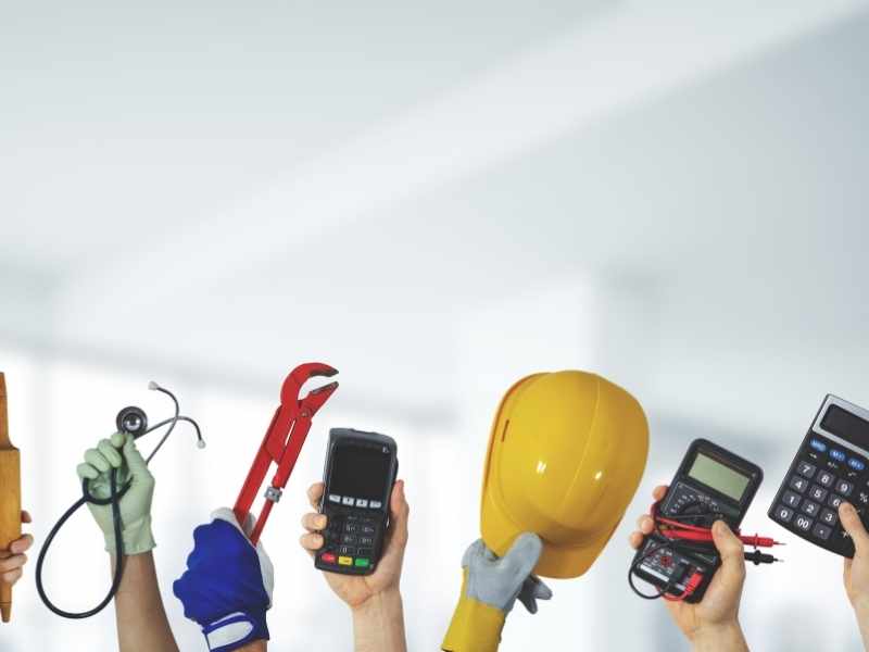 Hands holding work tools and devices, including a hard hat and a smartphone, representing expanded access to resources.