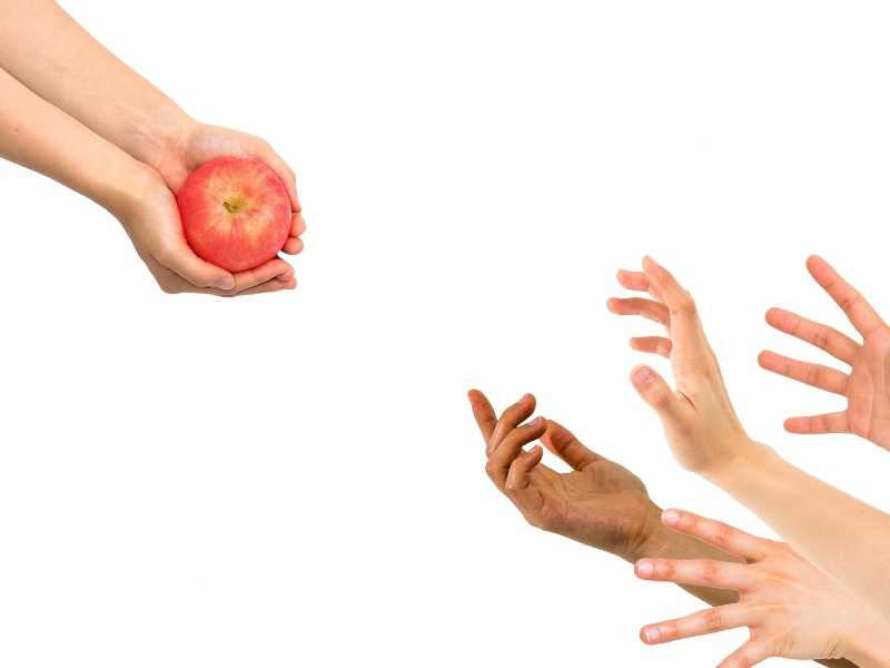Multiple hands reaching toward a single apple, symbolizing scarcity and demand outpacing supply.