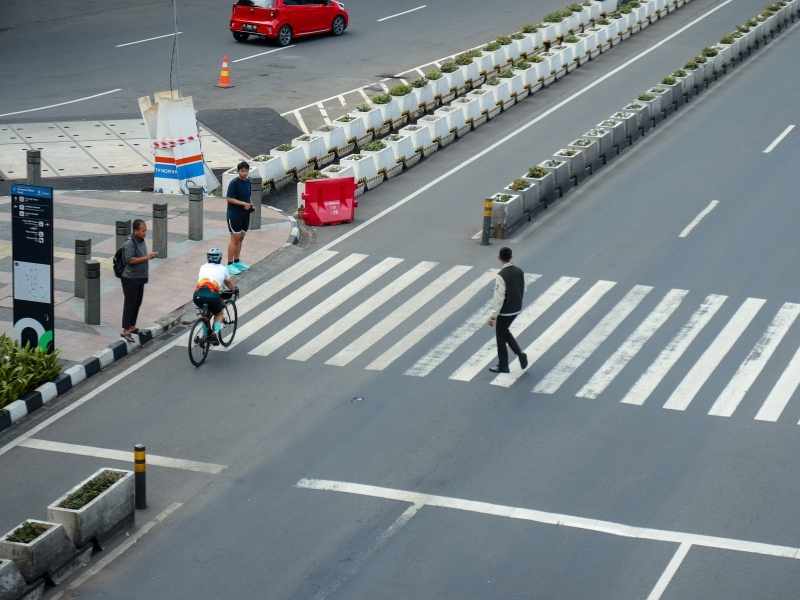 Overhead view of a wide zebra crosswalk and a protected bike lane with pedestrians crossing.
