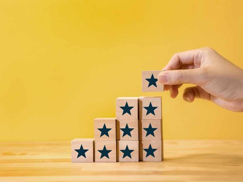 Hand placing a wooden block on a growing stack, symbolizing gradual progress.