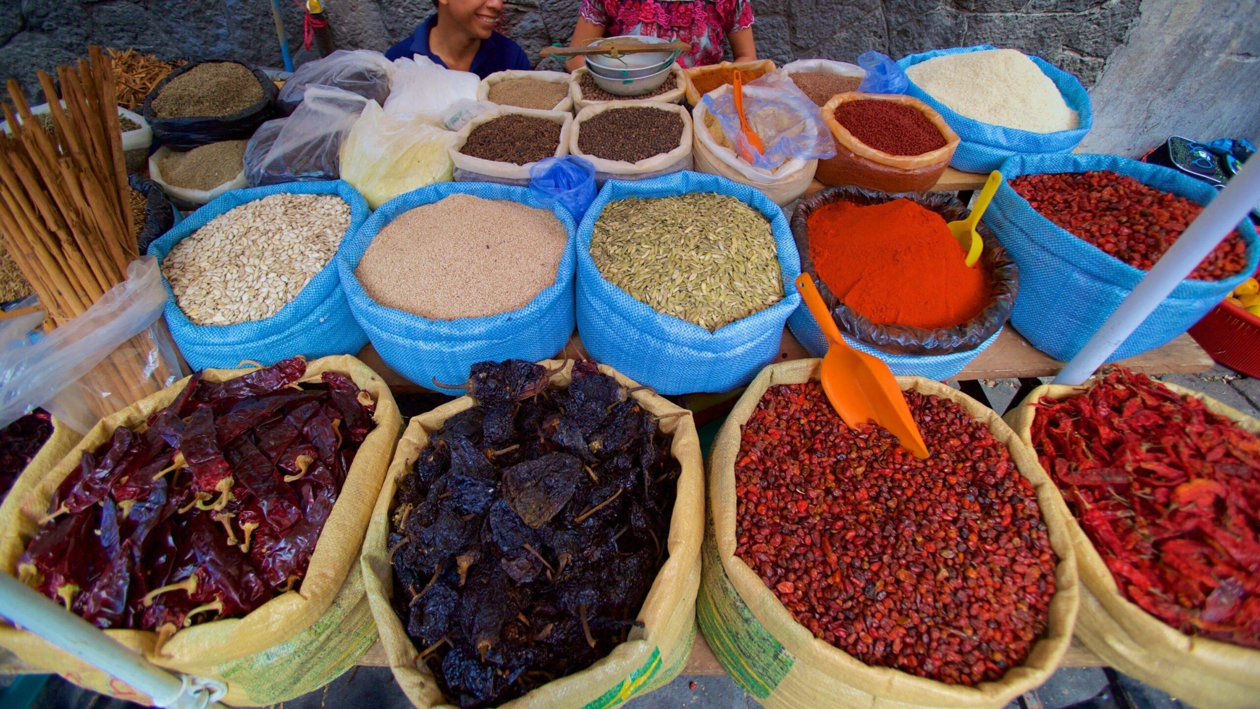 Colorful market stalls displaying fresh vegetables, dried peppers and traditional ingredients used in Guatemalan cuisine.